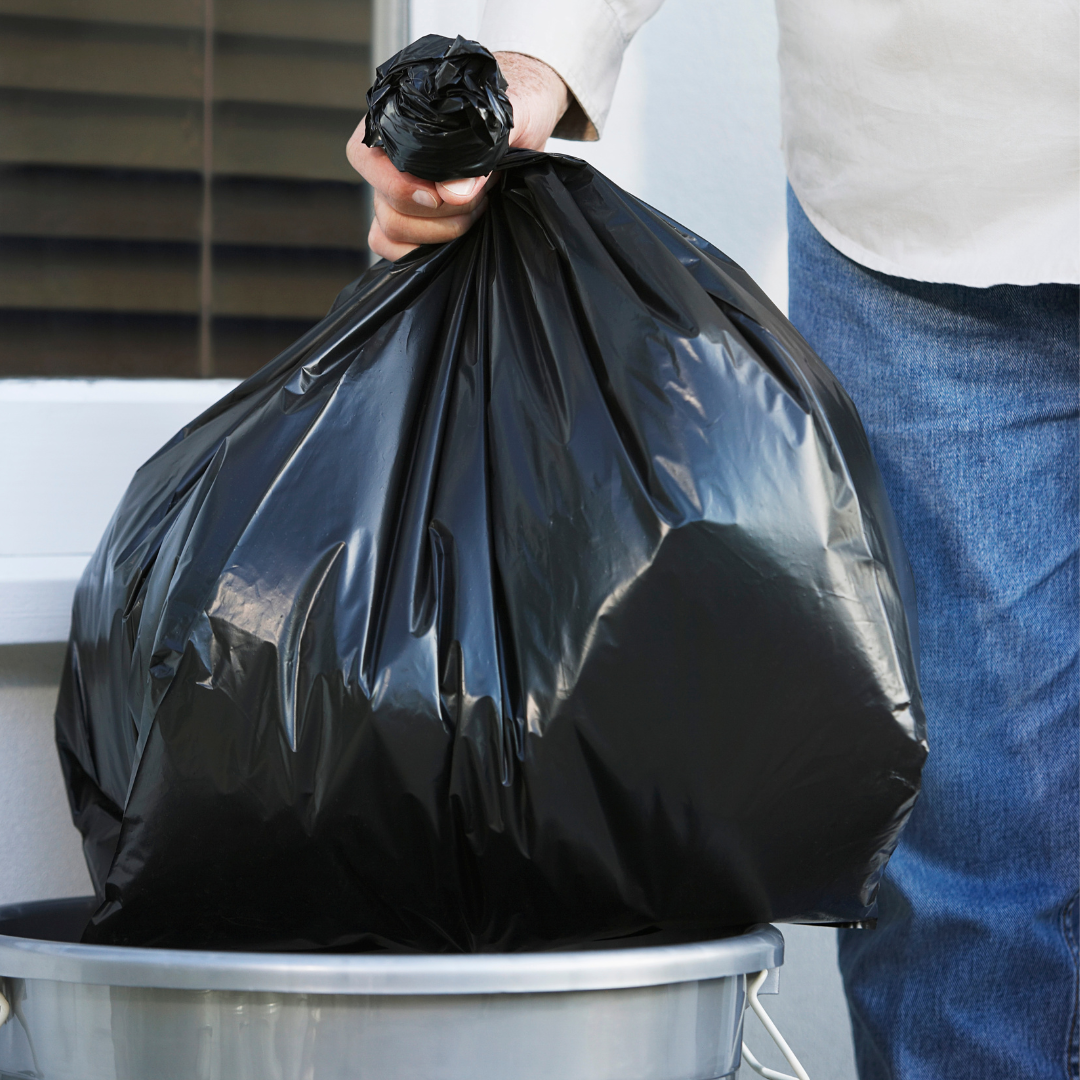 Black trash bag being placed in an extra trash bin outside