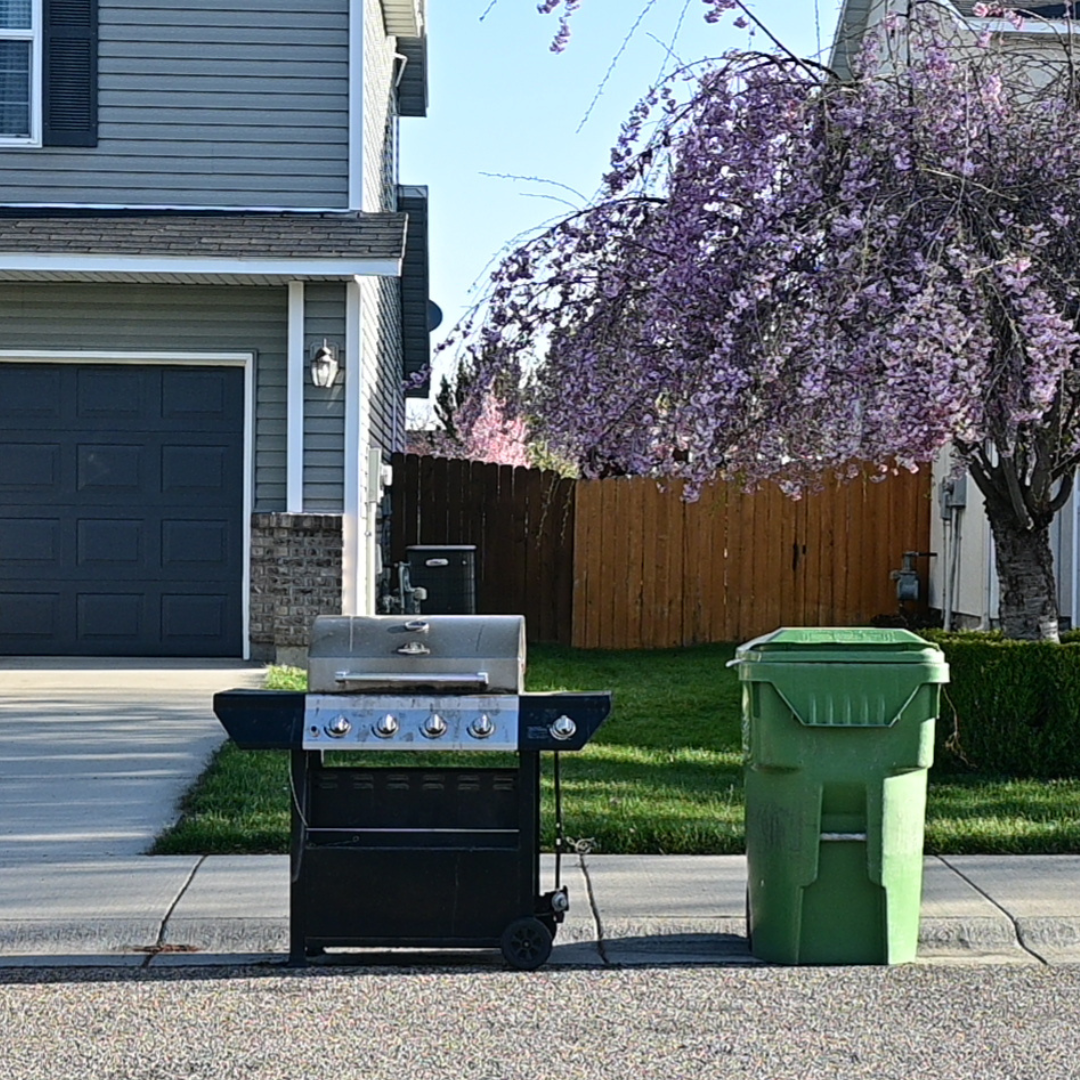 An old grill and a green garbage cart at the curb