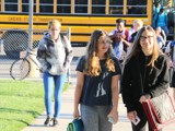 Kids walking to school from a school bus in the background.